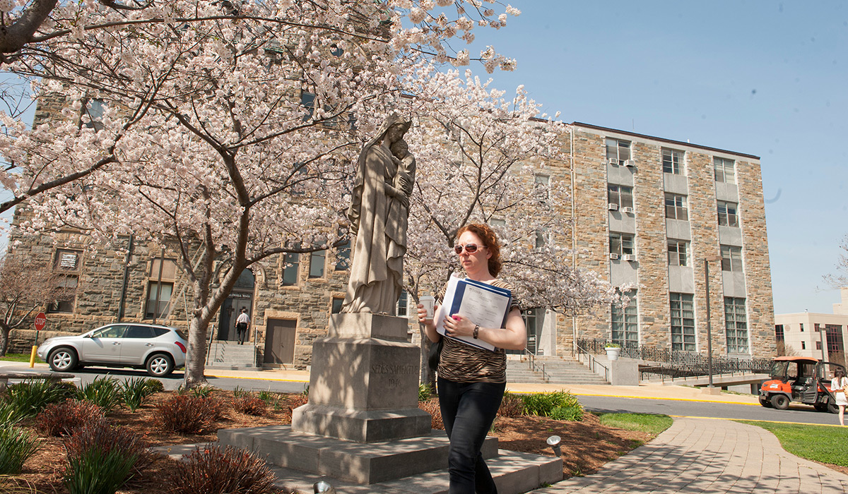 Student walking with books in front of statue of Mary